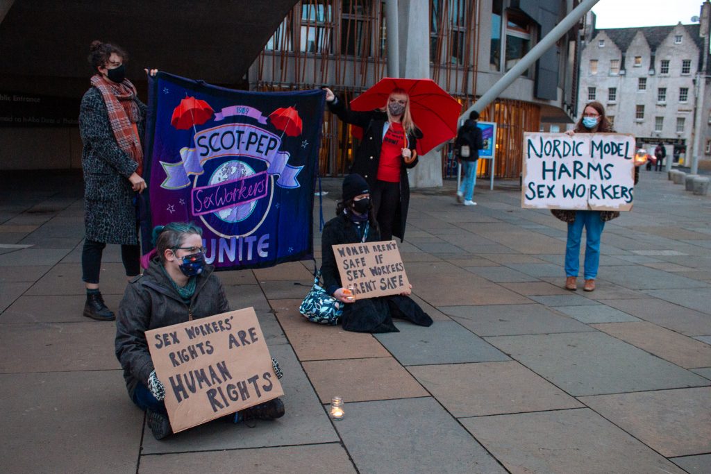 People gathered at the Scot Pep vigil, holding signs and a red umbrella